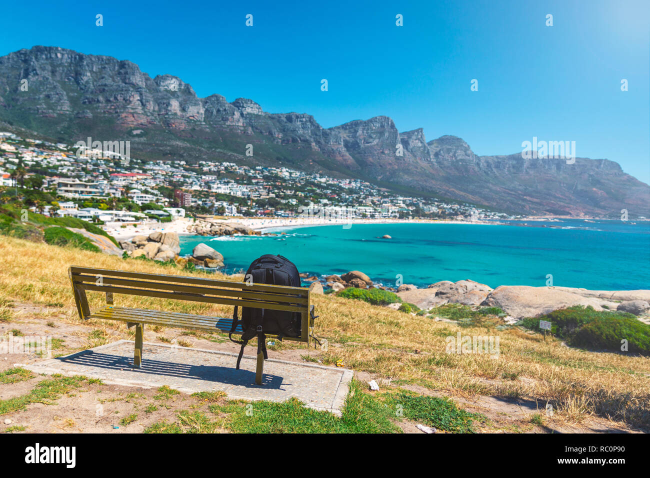 Backpack of lonely traveller on a bench with a view of Camps bay beautiful beach in Cape Town, South Africa Stock Photo