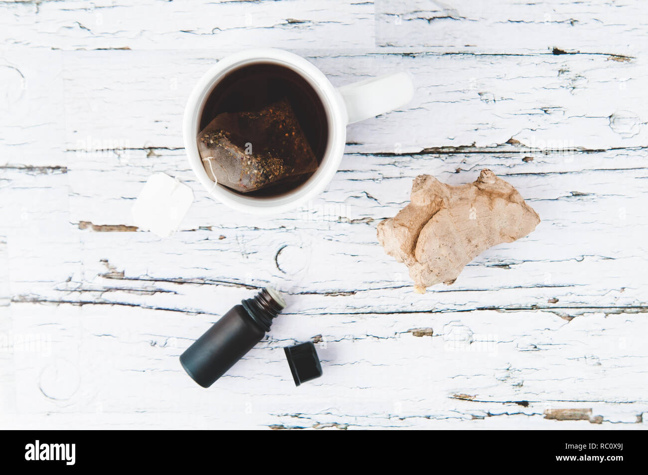 essential oil bottle, ginger root and a cup of tea on a white wooden background Stock Photo