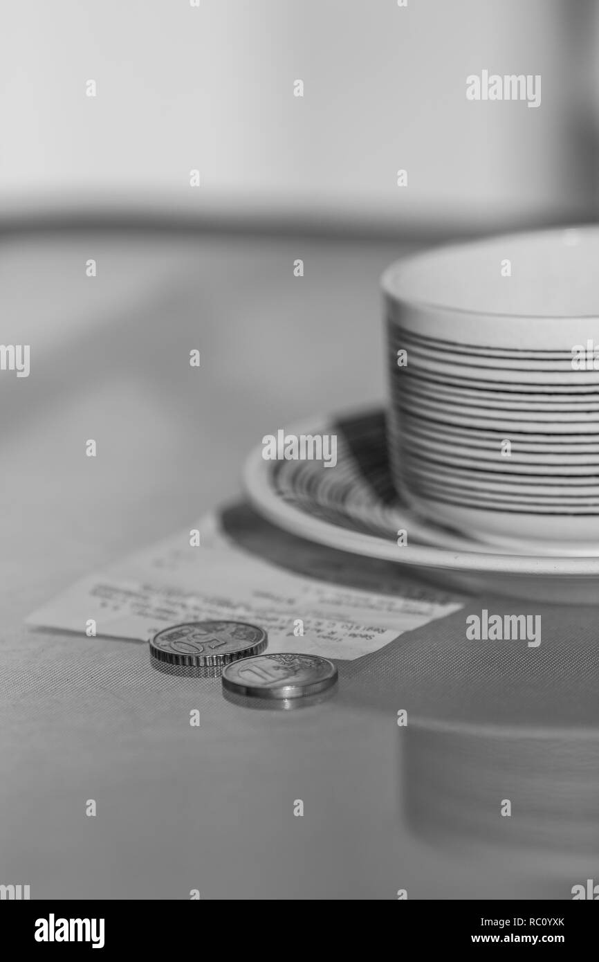 Black and white photo of coins, receipt and cup on glass table. Stock Photo