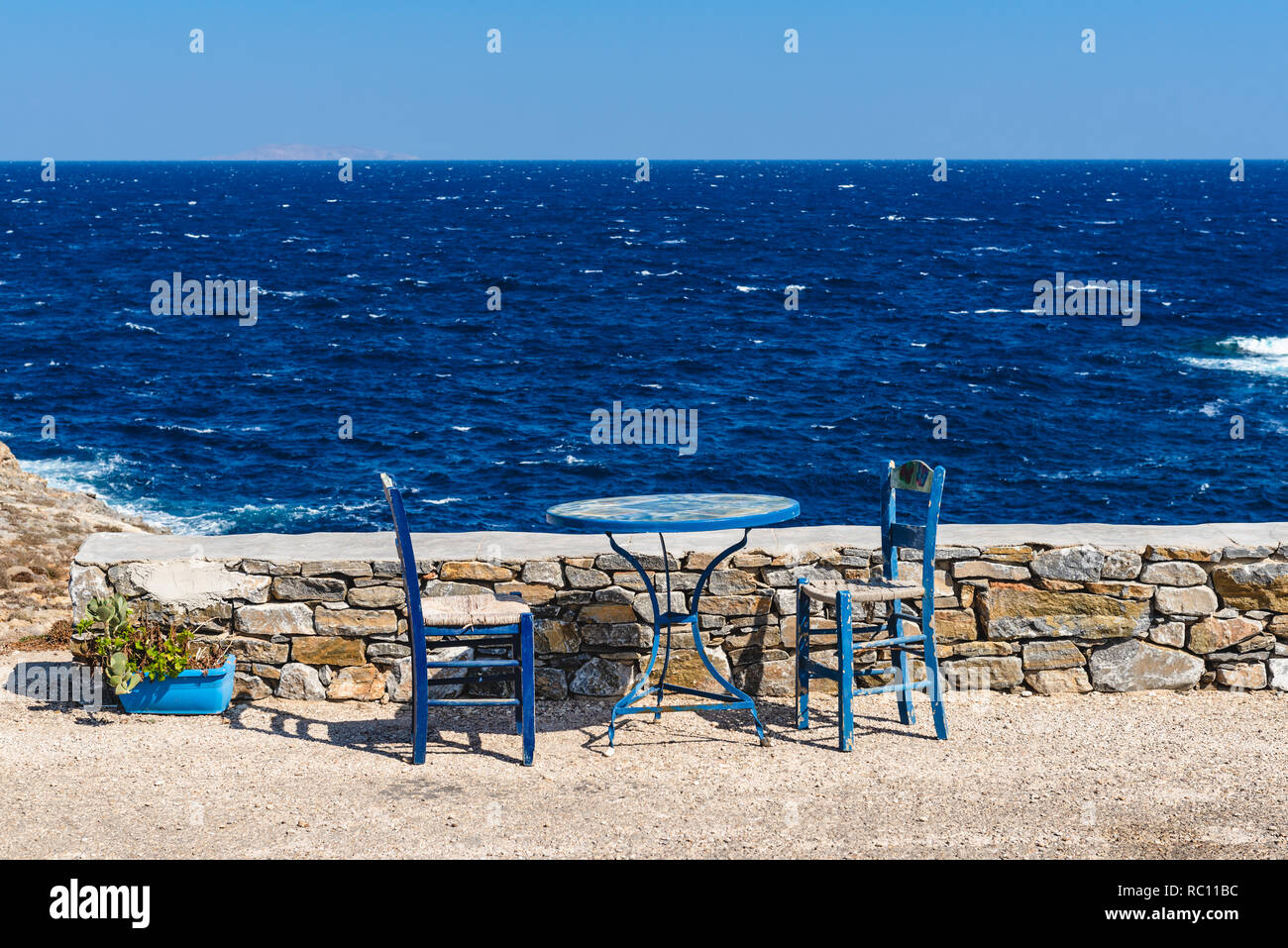 Table and chairs overlooking the sea. Cheronissos village at the north edge of Sifnos. Cyclades islands, Greece Stock Photo