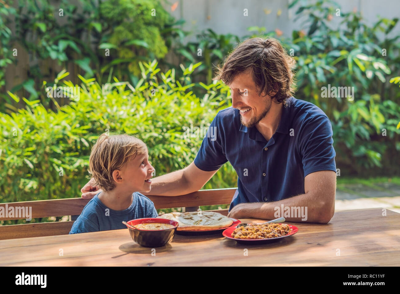 Father and son try Indian food in a cafe on the street. Stock Photo