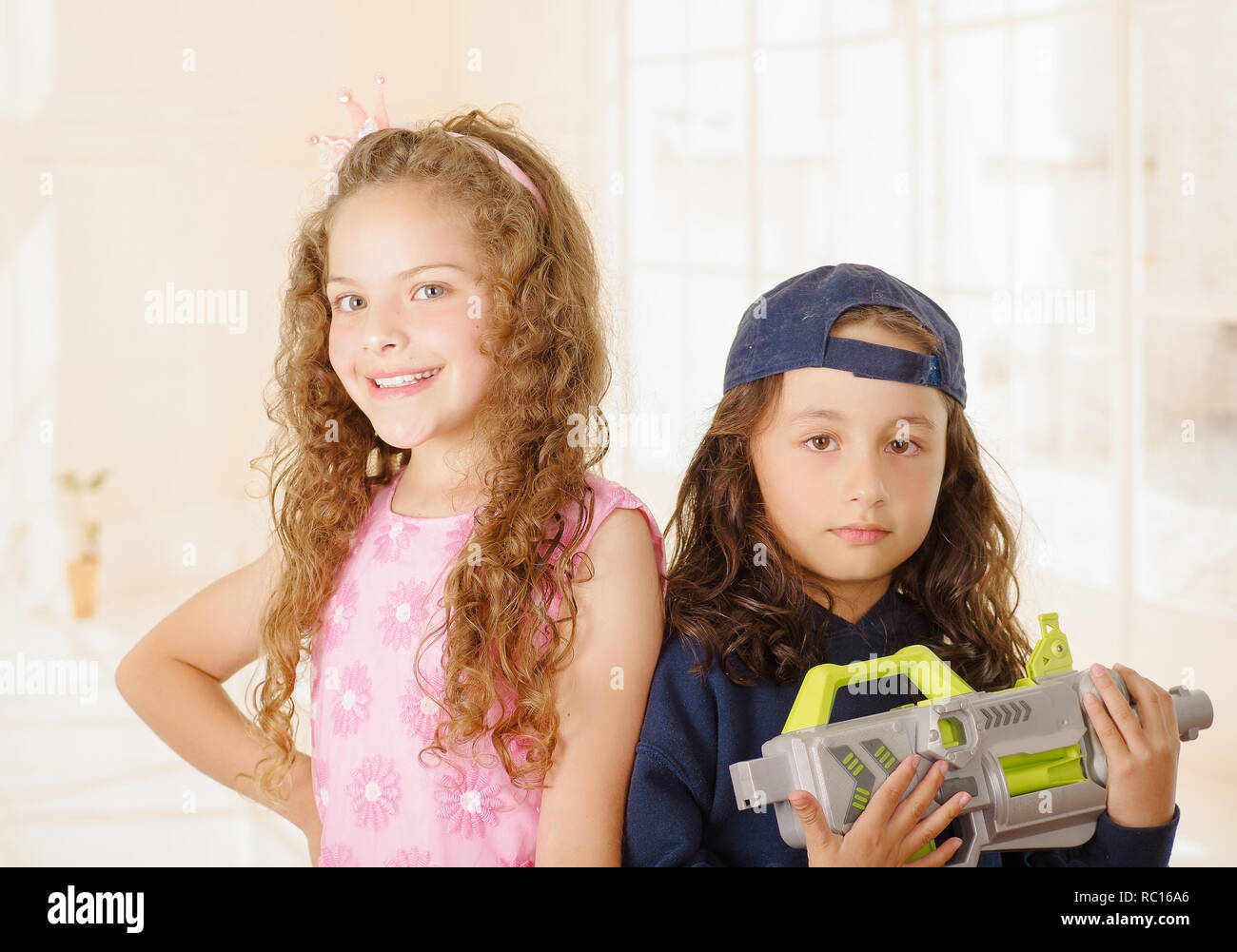 Close up of two girls one is wering boy clothes and holding a gun and other girl is wearing a pink princess dress Stock Photo