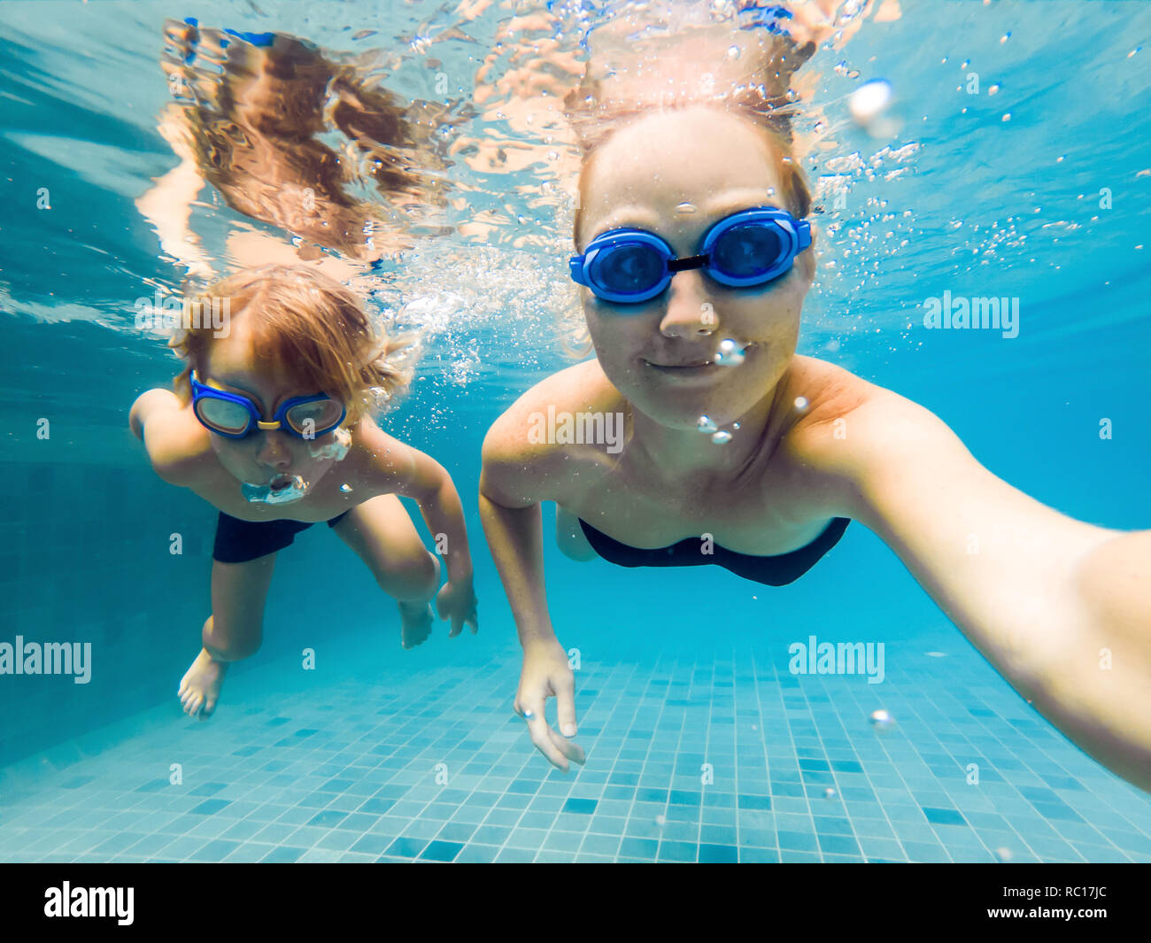 Mom and son in diving glasses swim in the pool under the water Stock