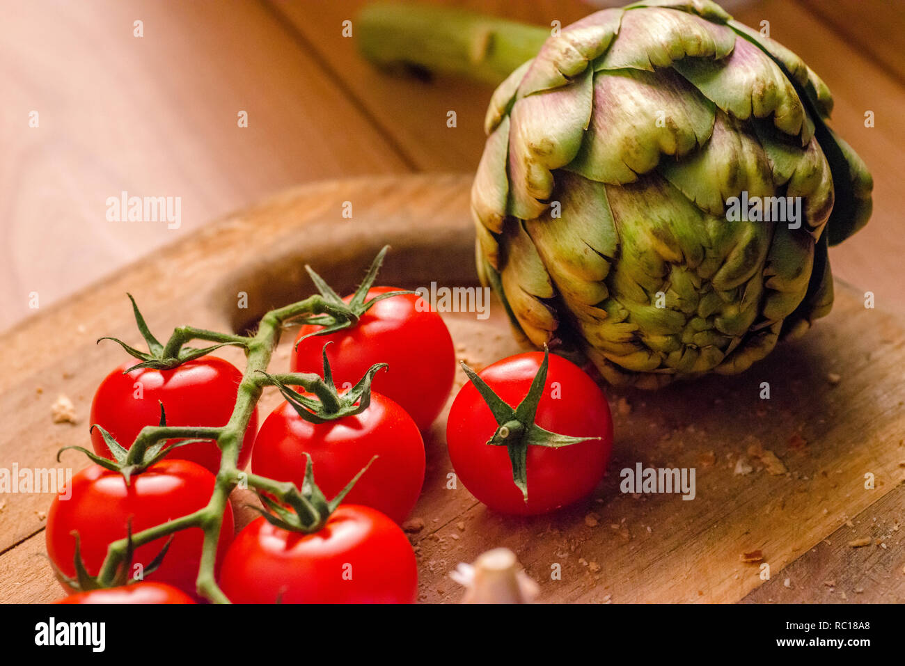 Truss tomatoes and an artichoke on a wooden chopping board Stock Photo ...
