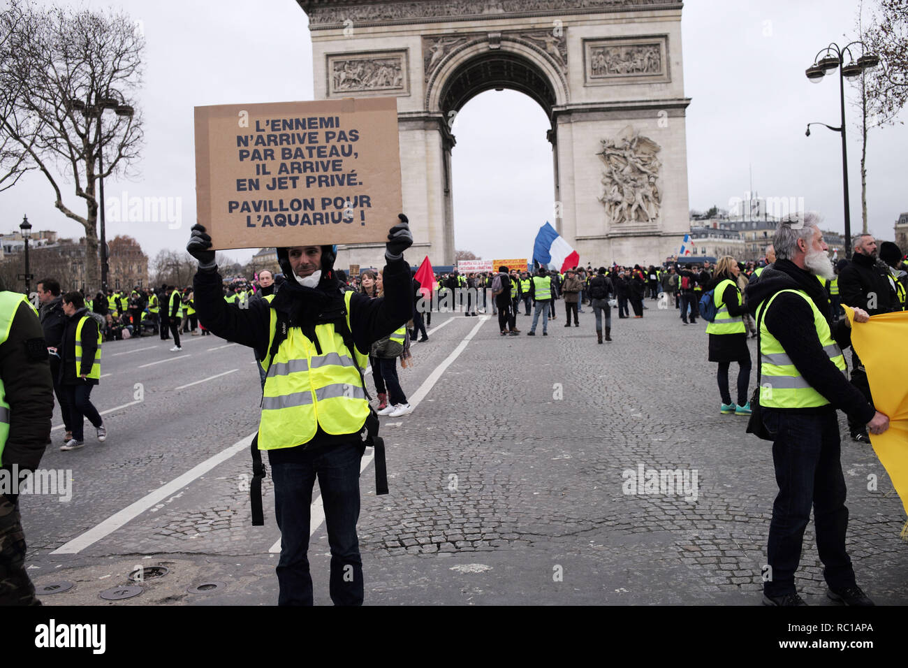Paris, France. 12th January, 2019. Gilets Jaunes, Yellow Vests,  demonstrators, are walking and showing their signs and complains "The Enemy  is not coming on boats, he's coming on private jets, give the