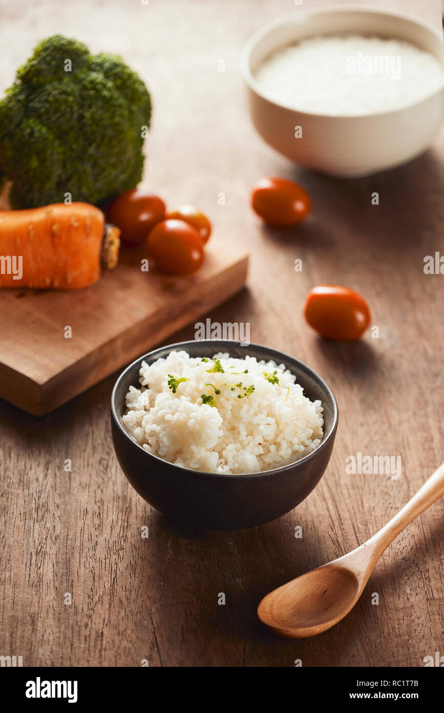Grains of rice in a wooden bowl and ingredients for a vegetarian recipe healthy eating concept