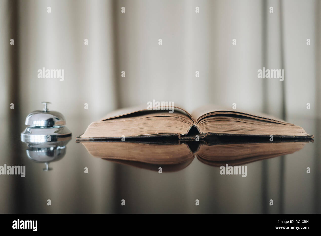 Opened old book and bell with reflected in brown surface. Hotel time Stock Photo