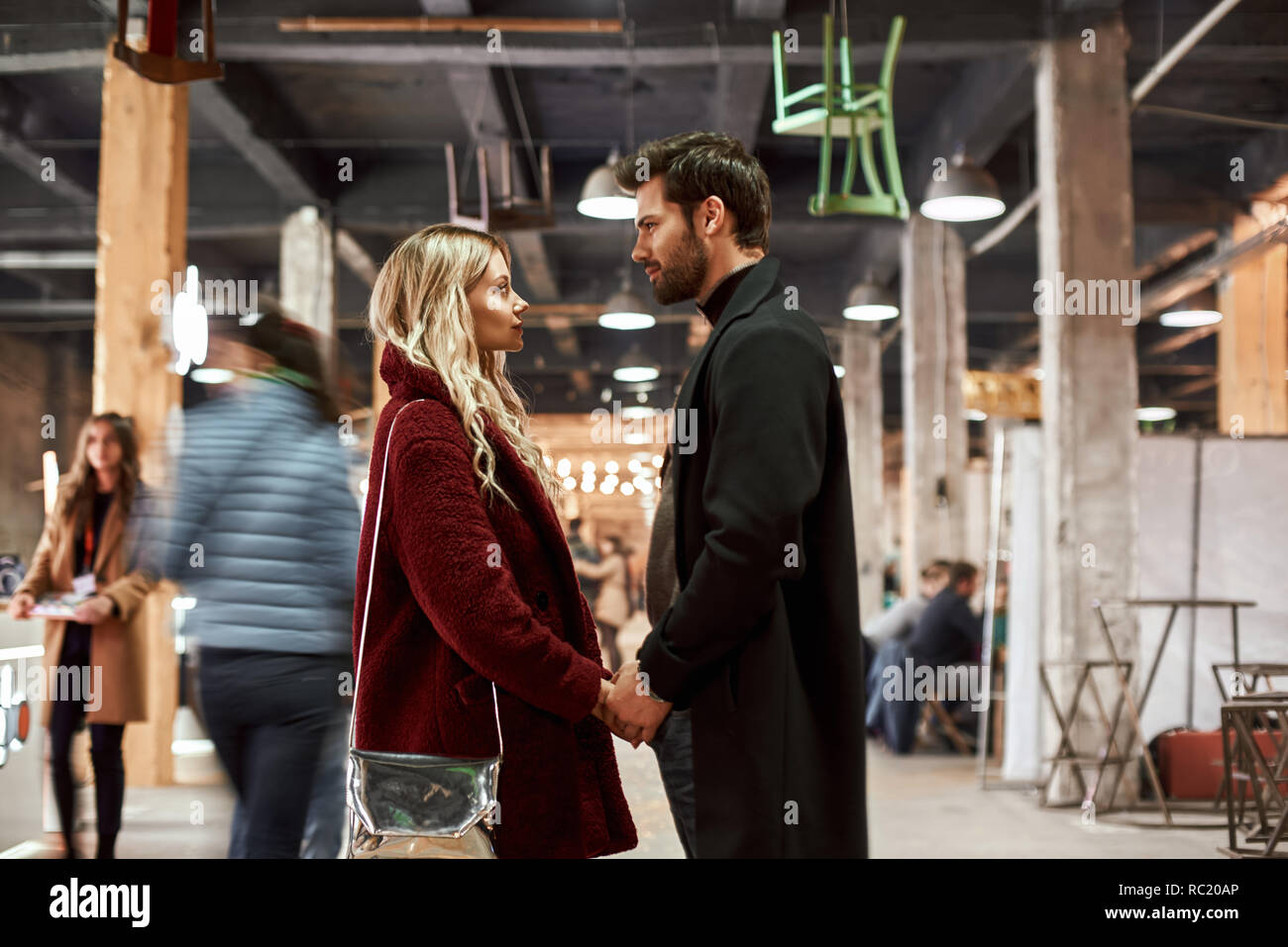 Holding hands together. Happy young joyful couple standing in rows at small street market. Autumn season, blond haired woman holding hands of her boyf Stock Photo