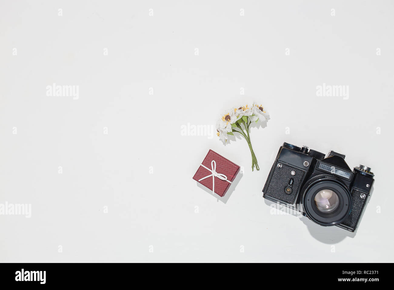 Minimalistic flat lay composition with retro camera, vinous gift box and spring field flower on white background. Trendy flat lay mockup for bloggers, designers, photographers, etc. Stock Photo