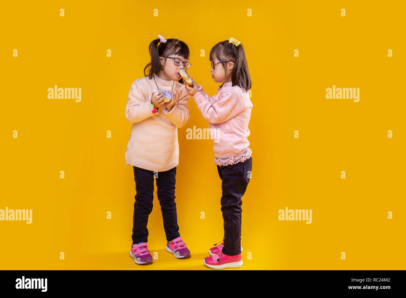 Cute little girl carrying puffy donut while her sister sniffing it Stock Photo