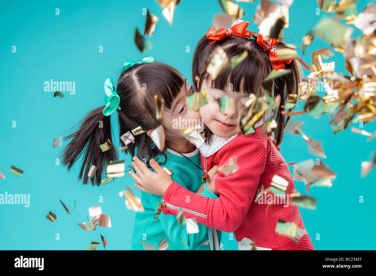 Dark-haired positive sisters kissing each other while standing Stock Photo