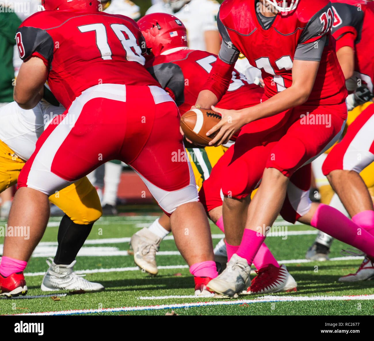 Quarterback turning to look for someone to hand off the ball to just after the snap during a high school football game Stock Photo