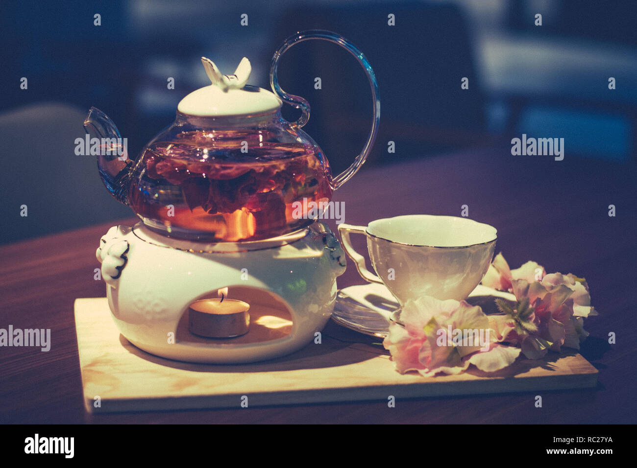 flower petal tea in a glass tea set with tea warmer light Stock Photo