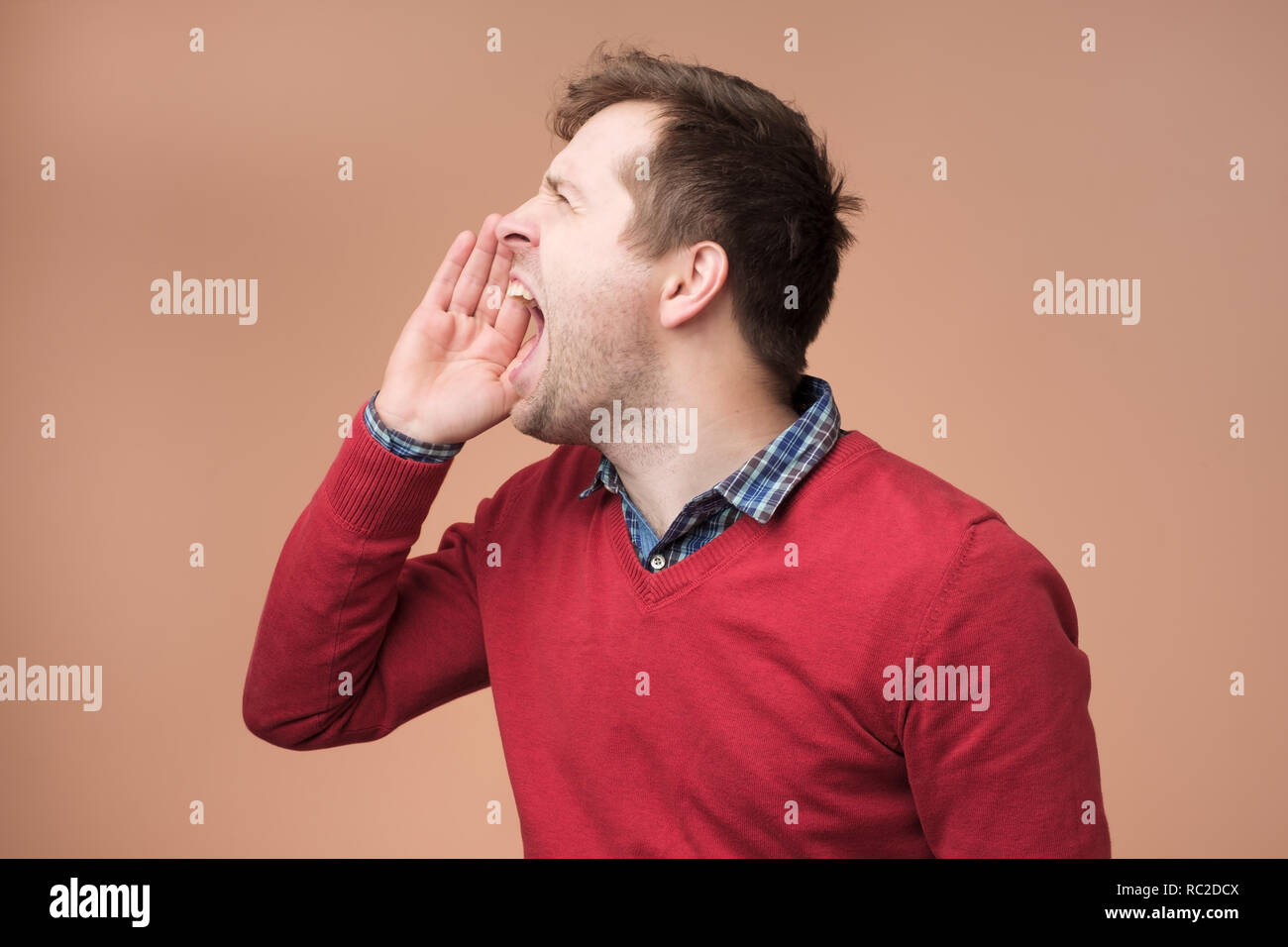 Closeup side view profile, portrait of mad young man, worker, business employee with wide opened mouth, yelling, isolated on brown background. Stock Photo