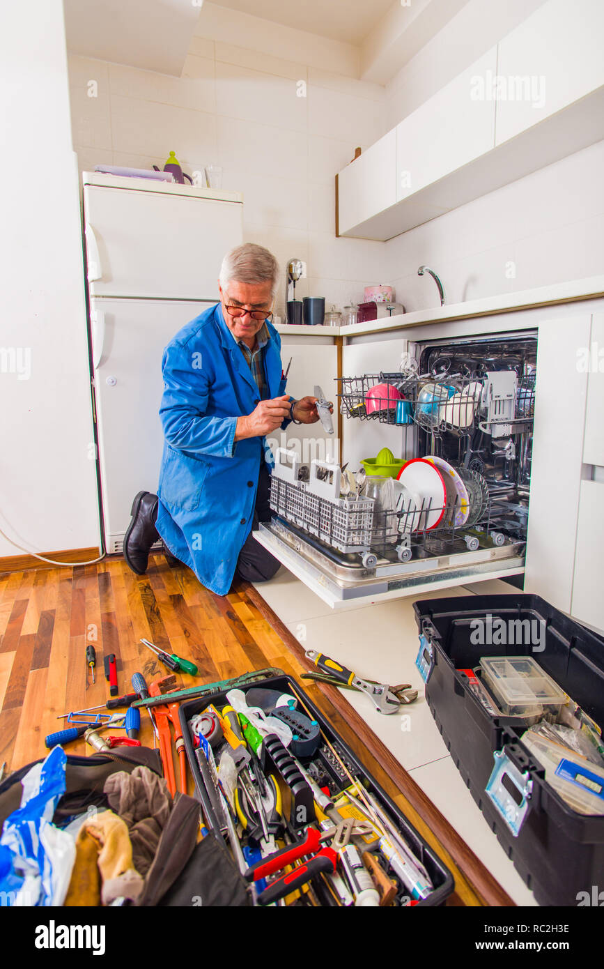 Mature handyman is opening the dishwasher in the kitchen with the tool