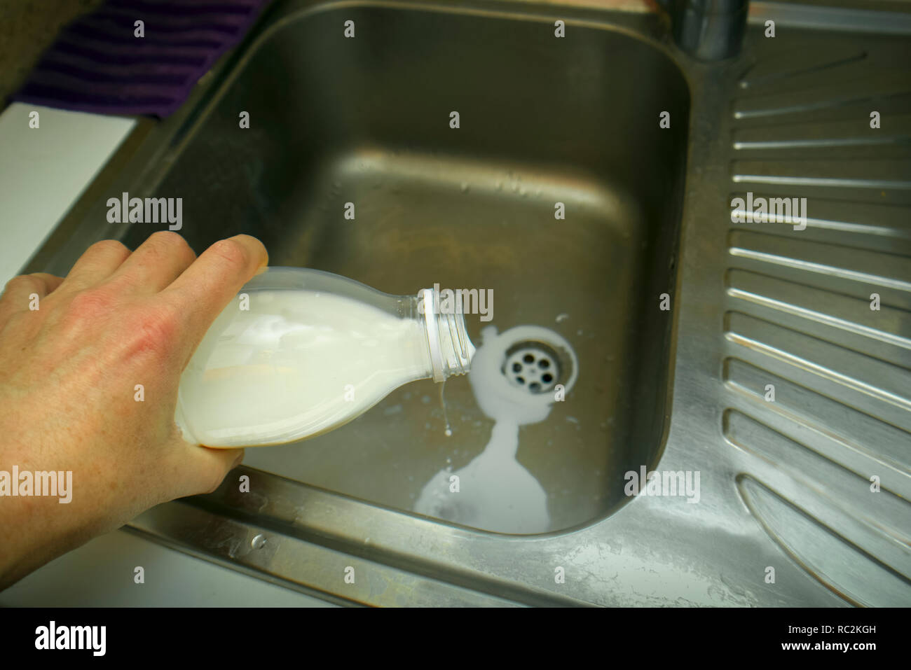 A hand with bottle of milk seems gone off over a kitchen sink Stock