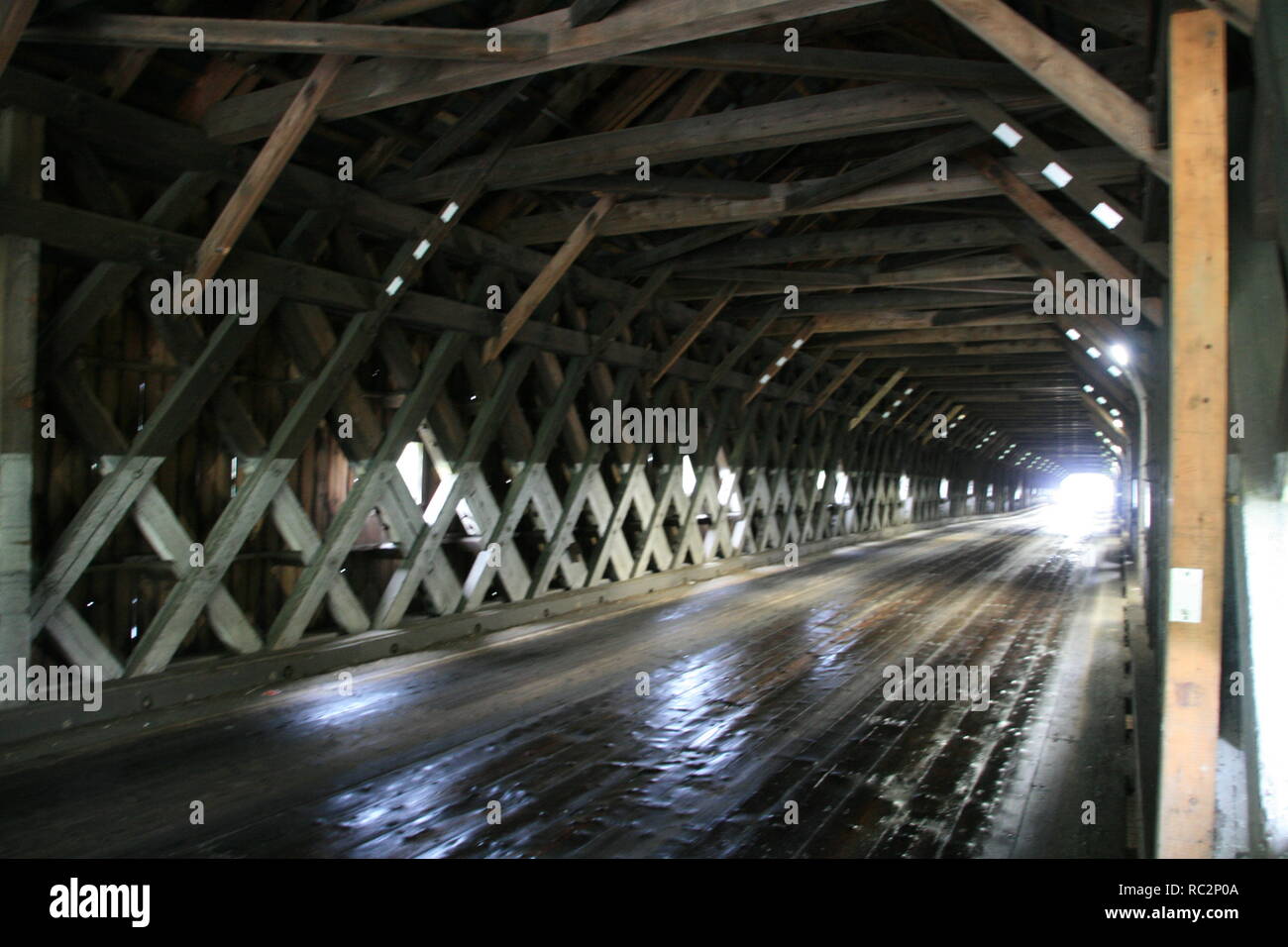 Interior view of Cornish Windsor Covered Bridge (New Hampshire/ Vermont ) showing detailed wooden frame construction & car headlights in distance Stock Photo