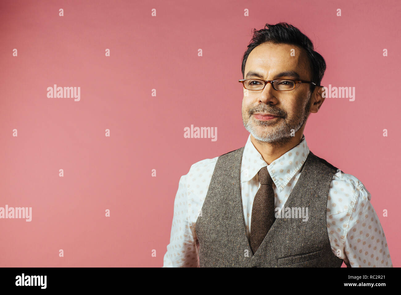 Portrait of a mature man in vest and glasses looking off camera, isolated on pink Stock Photo