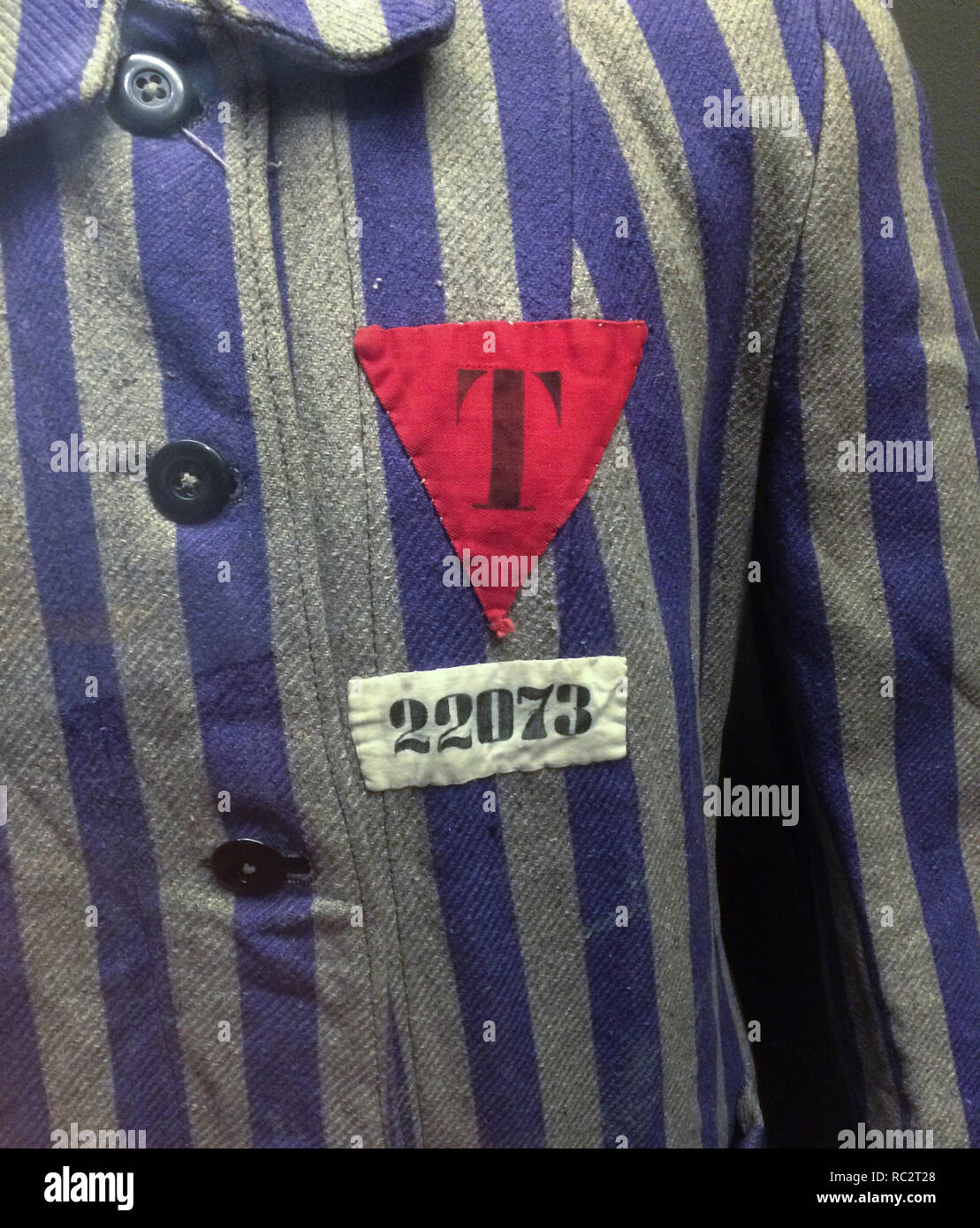 Red triangle on striped uniform used in Nazi concentration camps during World War II on display at the exhibition 'Touches of Statehood' in Prague, Czech Republic. The badge is marked with letter 'T' meaning the political enemies of Czech nationality, from the German word 'Tschechien' for Czech. The exhibition devoted to the centenary of Czechoslovakia runs till 31 October 2018. Stock Photo