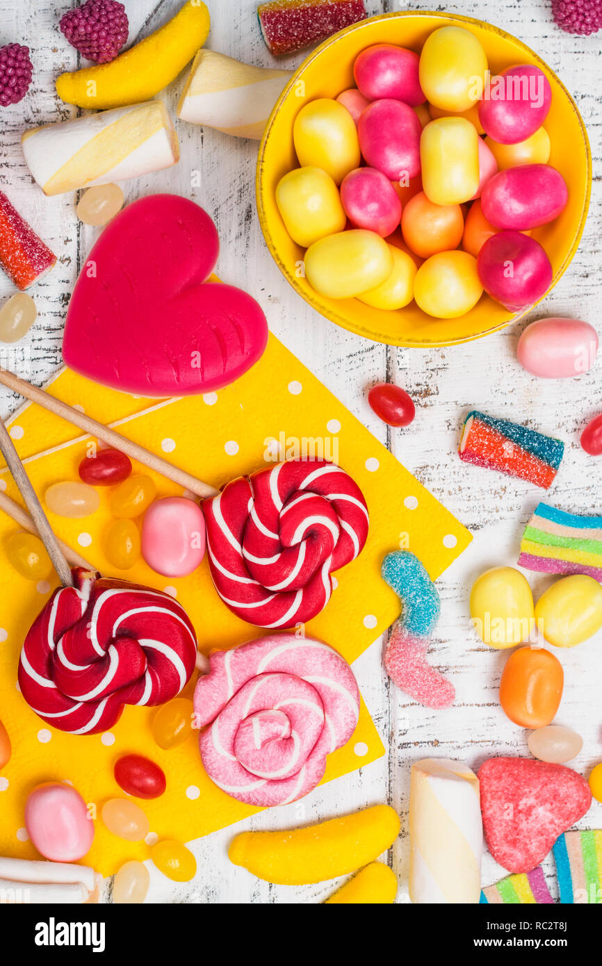 Pink candies, lollipops and jelly beans on white wooden background