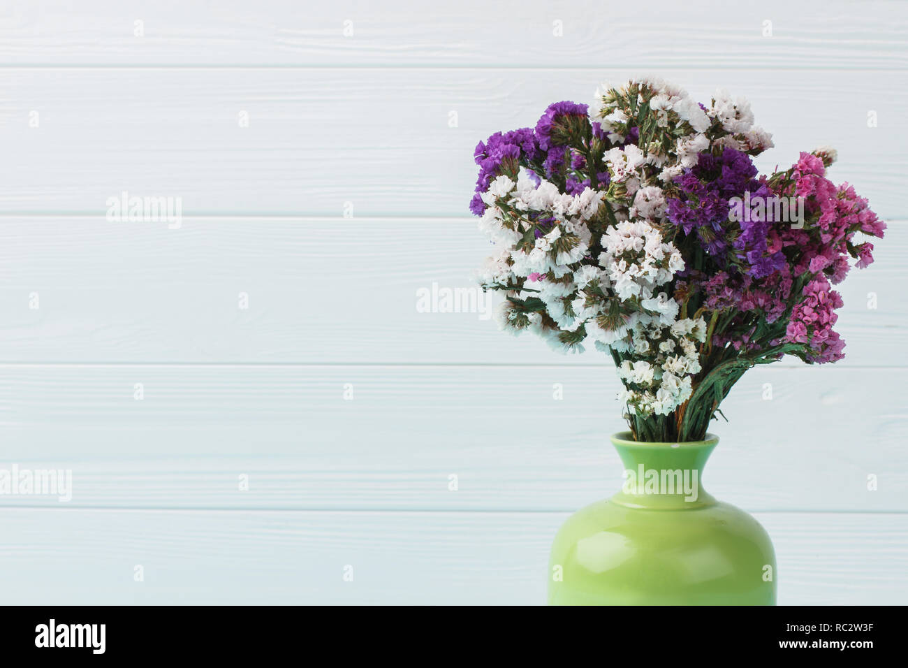Different statice limonium flowers in a green ceramic vase. Close up. Blue wooden background. Stock Photo