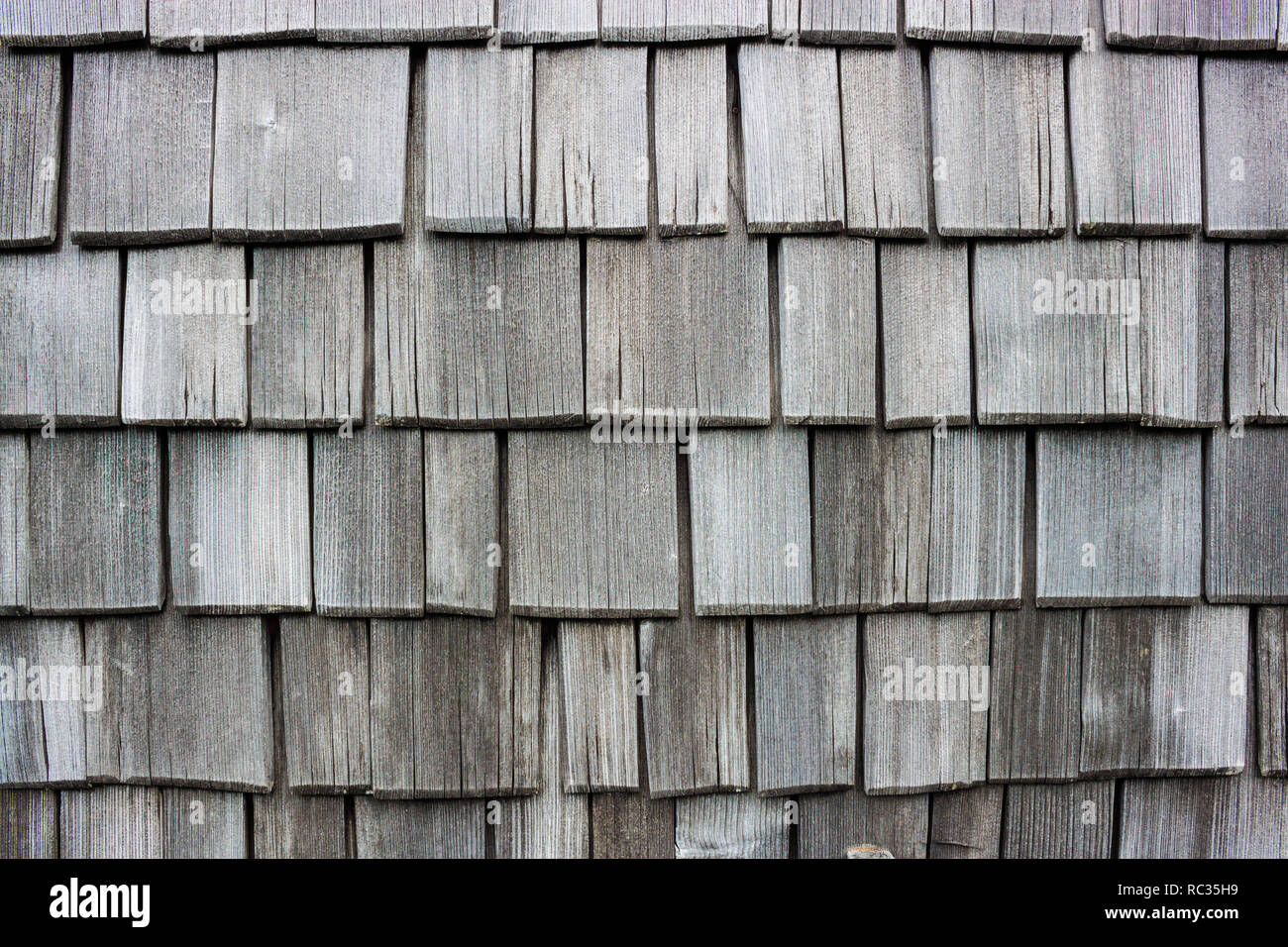 Wood shingle wall siding made of larch. Old, discolored and worn by weather shingles. Traditional austrian house siding. Stock Photo