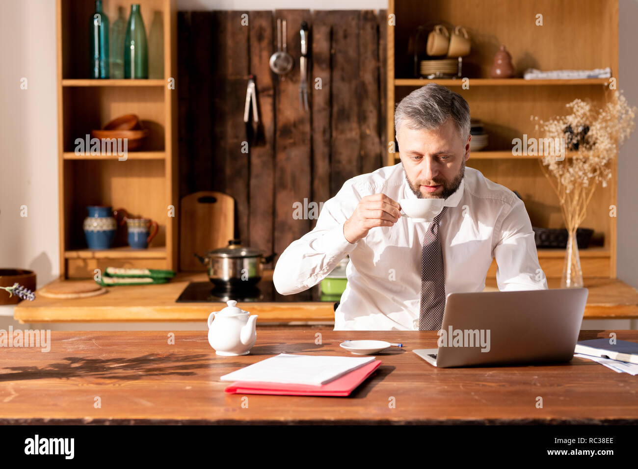 Pensive handsome man using laptop and drinking tea at home Stock Photo