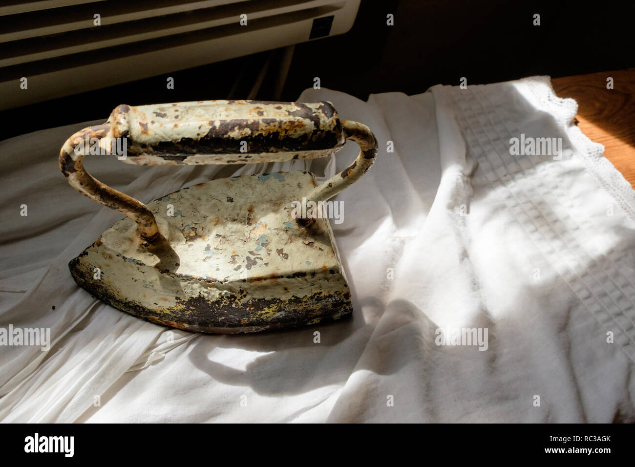 Antique rusted, worn and peeling stone clothes iron on white fabric. Stock Photo