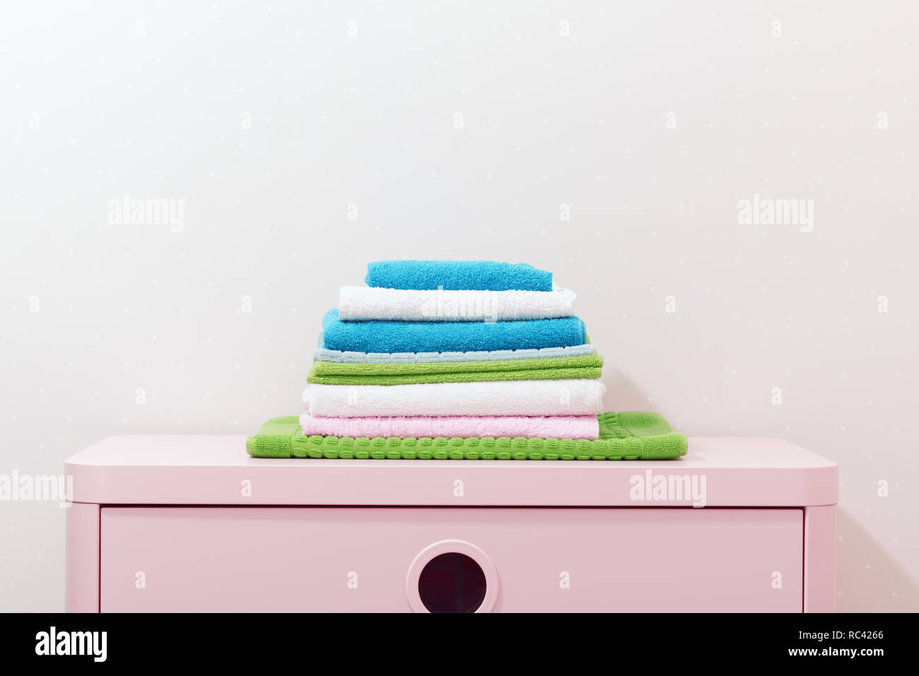 On the chest lies a stack of stacked colorful towels. Stock Photo