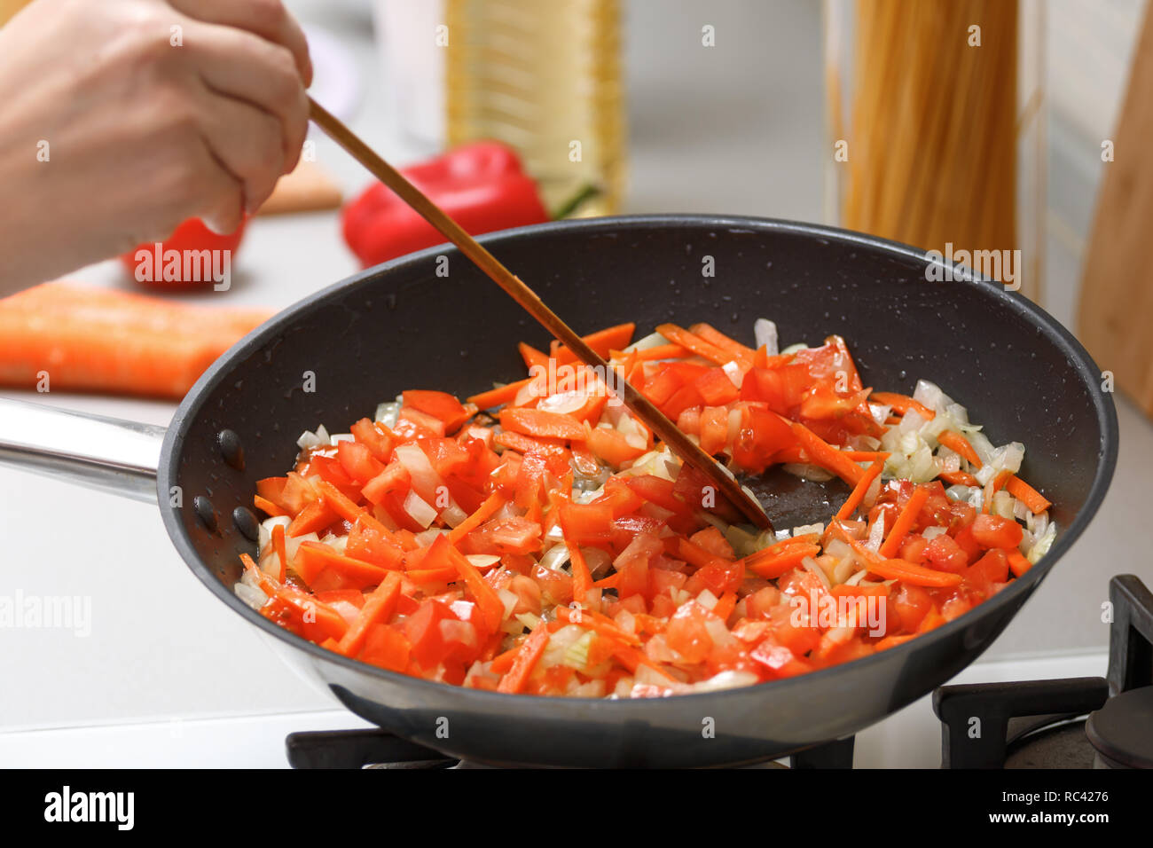 Homemade cooking. A woman fries onions, carrots and tomatoes in a hot pan with vegetable oil. Close-up. Stock Photo