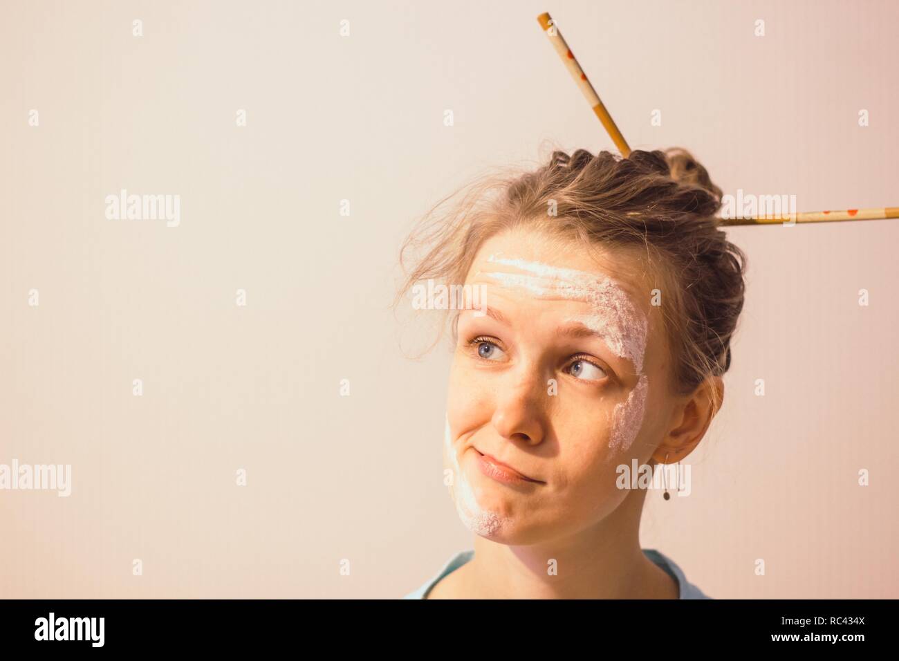 Girl with a soiled face flour and chopsticks in her hair on a white background. Girl with astonished look of face. Stock Photo