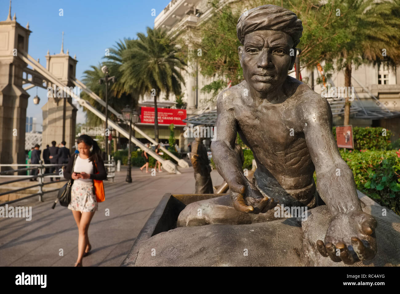A bronze sculpture in the People of the River series by the Singapore River, depicting a porter of old about to be handed a sack of goods; Singapore Stock Photo