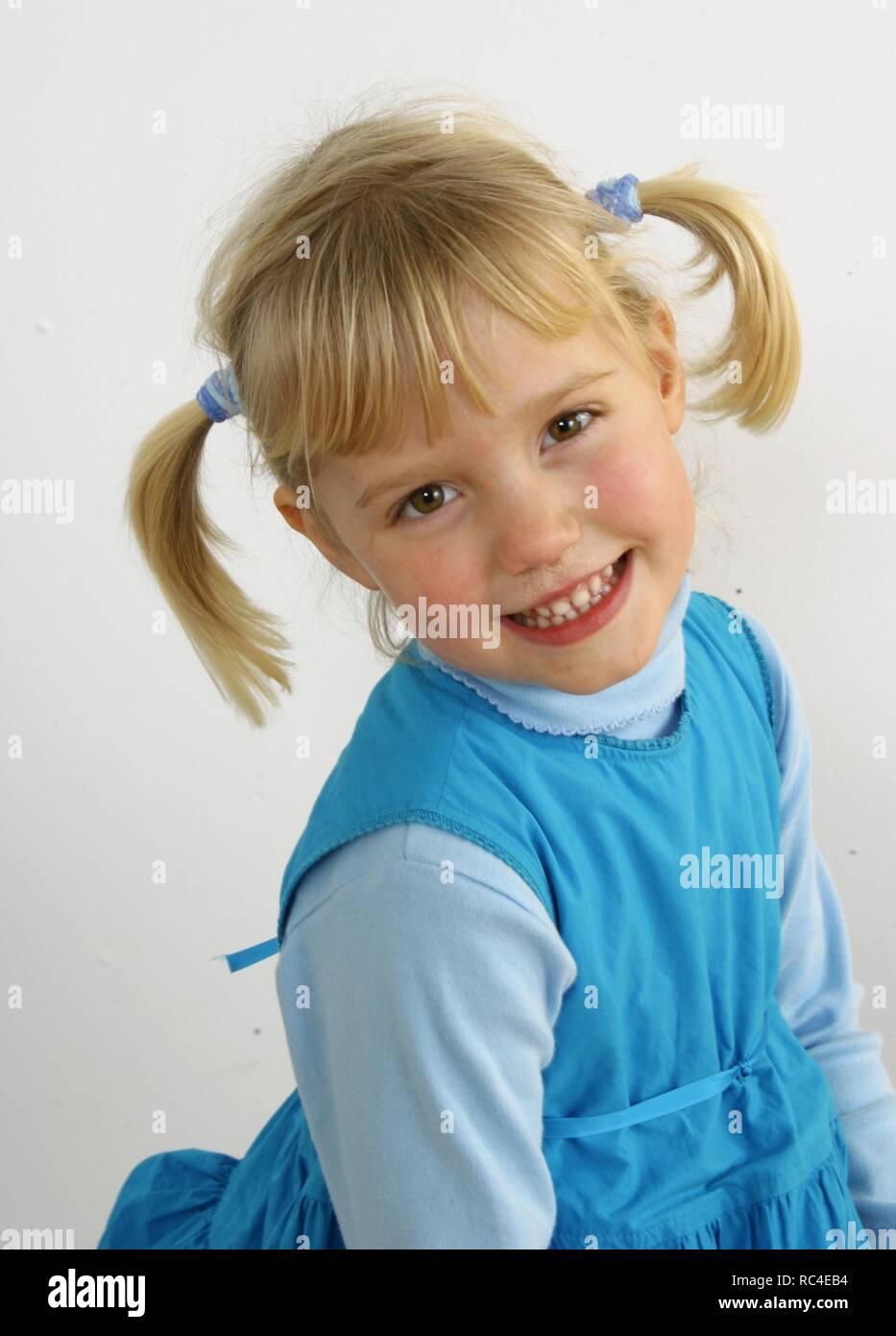 Sweet adorable little girl with straight blonde ponytails on her head wearing blue clothes. Happy portrait on white background. Stock Photo
