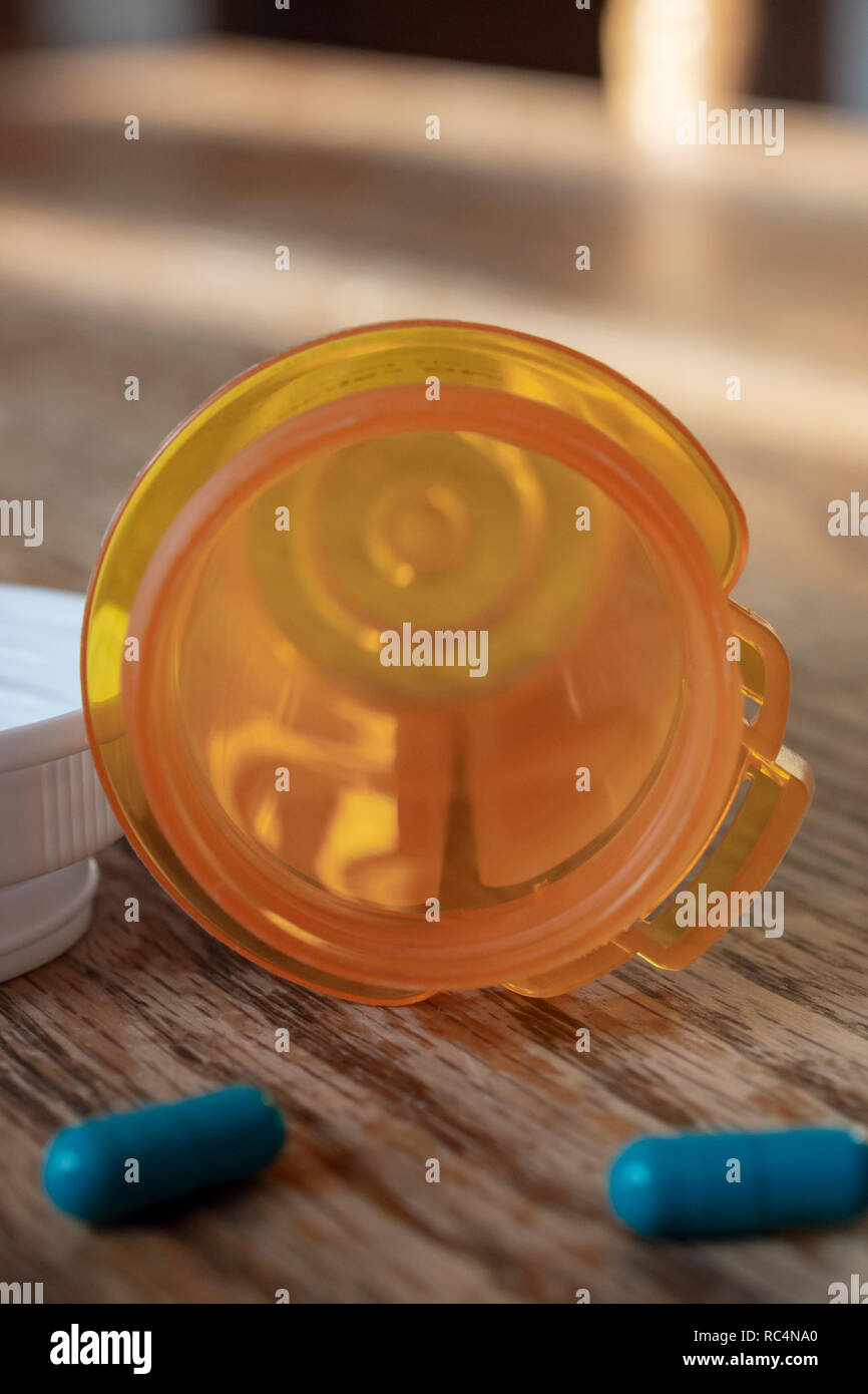 Nearly empty pill bottle with two blue capsuls in the foreground blurred.  On wooden table. Stock Photo