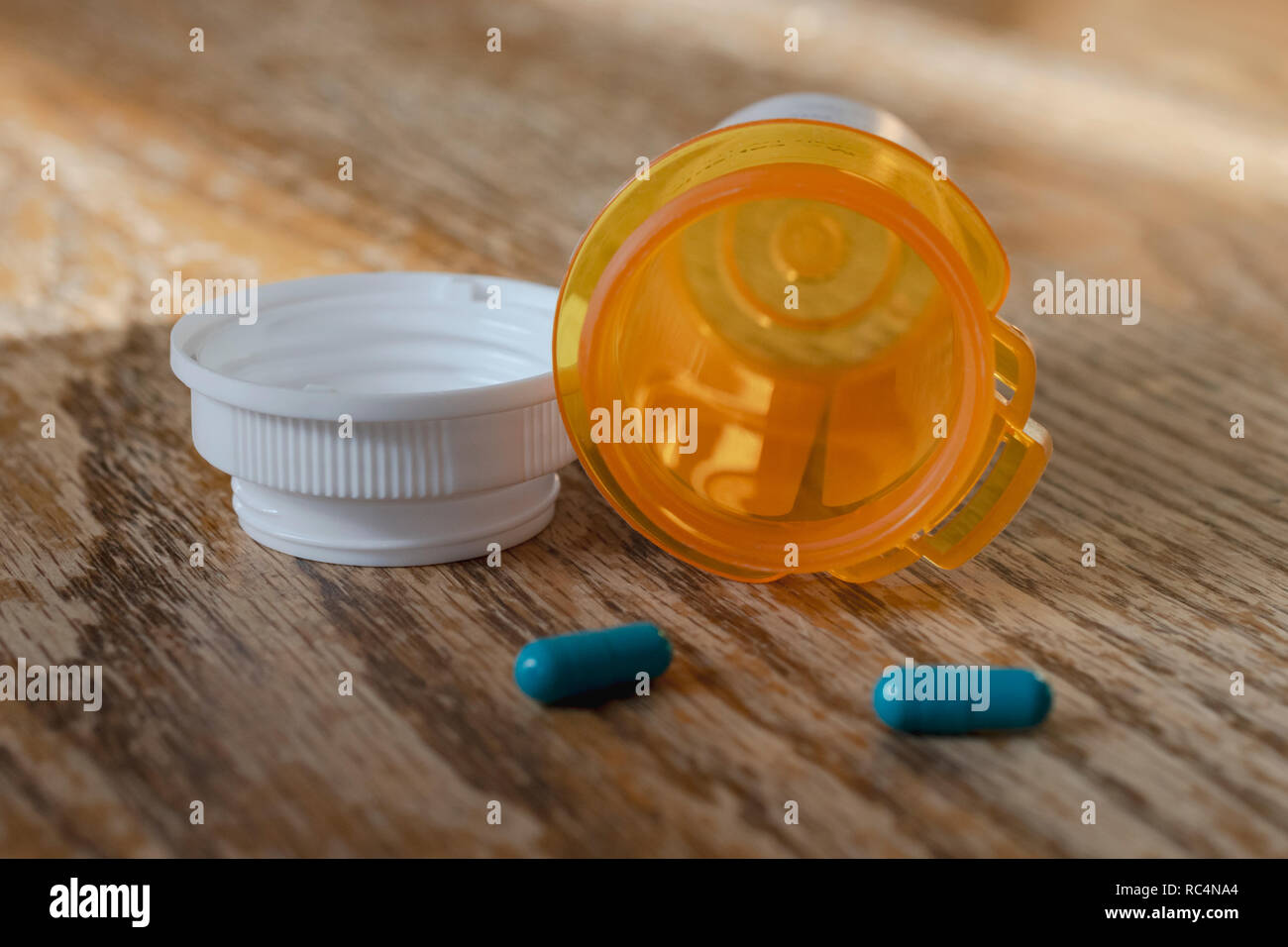Prescription pill bottle with last two blue pills spilling onto wooden kitchen table.  Close up view. Stock Photo