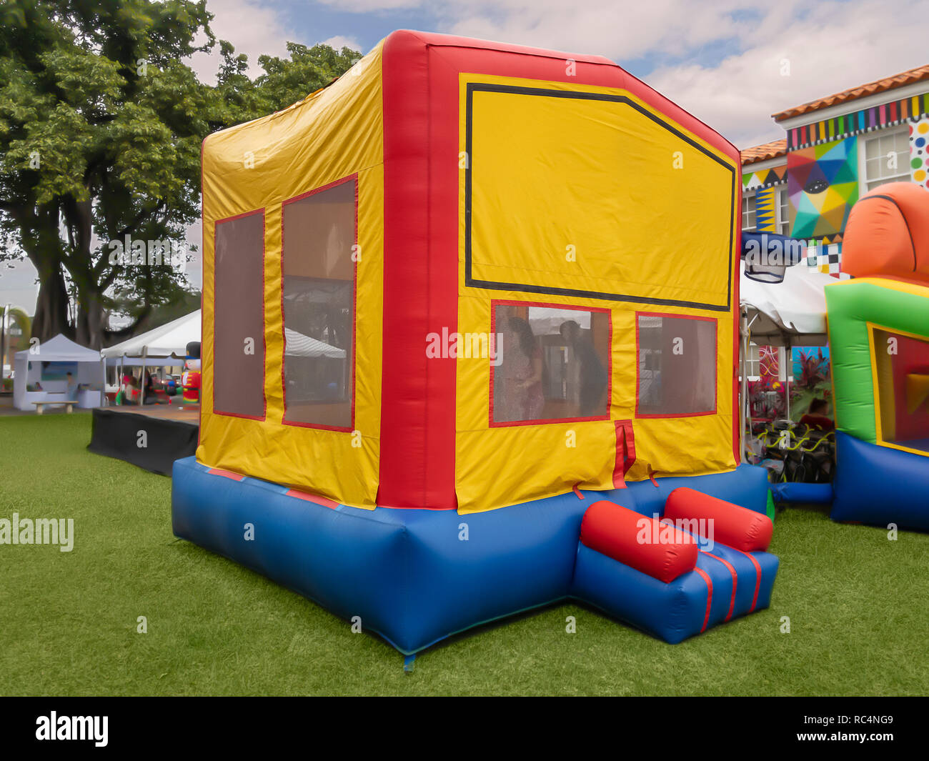The colorful bounce house on the green grass stands out for all the kids to see and enjoy at the community fair. Stock Photo