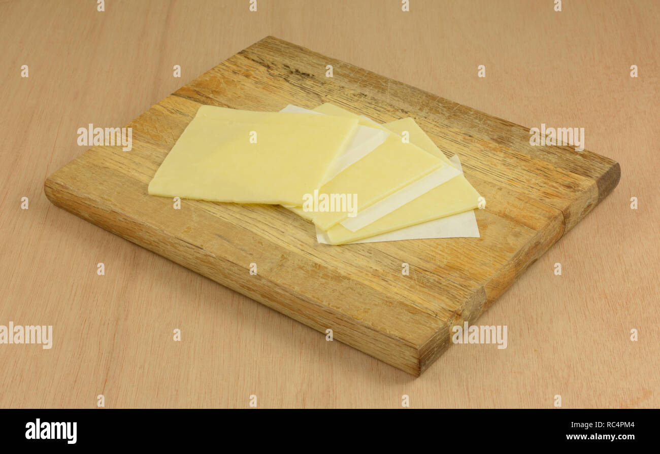 White cheddar cheese slices separated by paper on wooden cutting board in preparation for making food Stock Photo