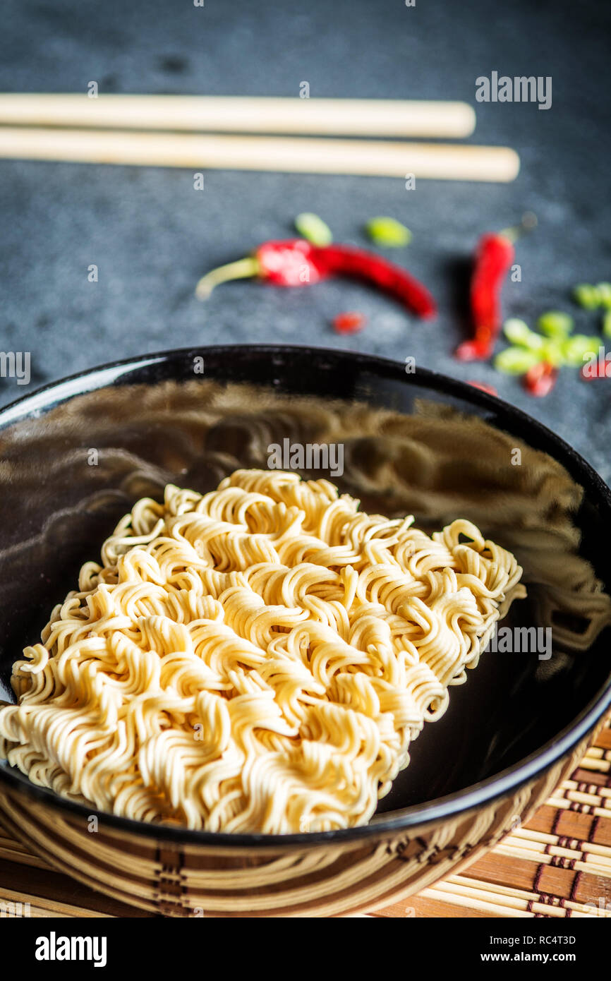Black bowl of asian instant noodles with and red chili peppers and green onion and chopsticks Stock Photo