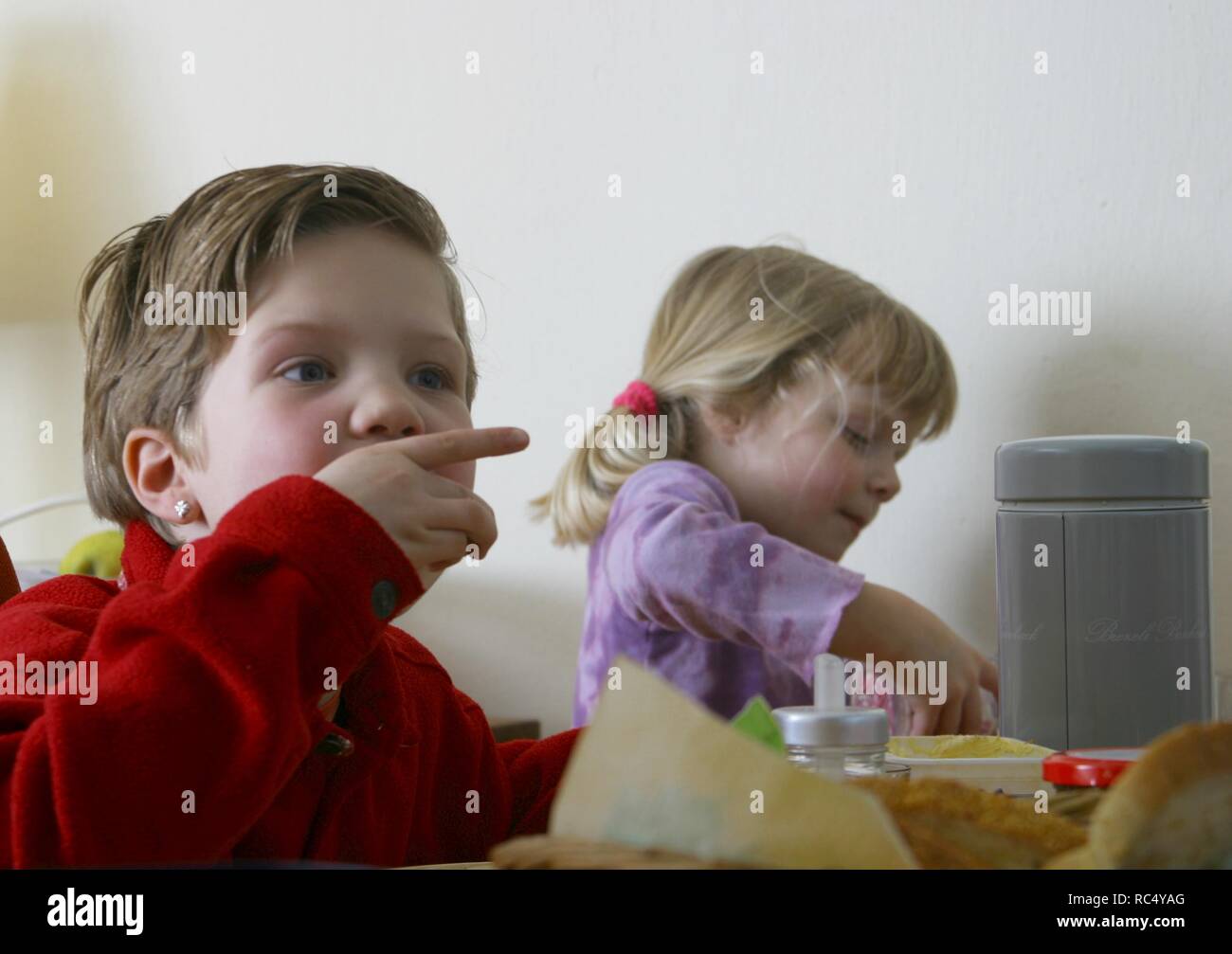 Two caucasian young self-dependant children eating lunch with hands at dining table indoors Stock Photo