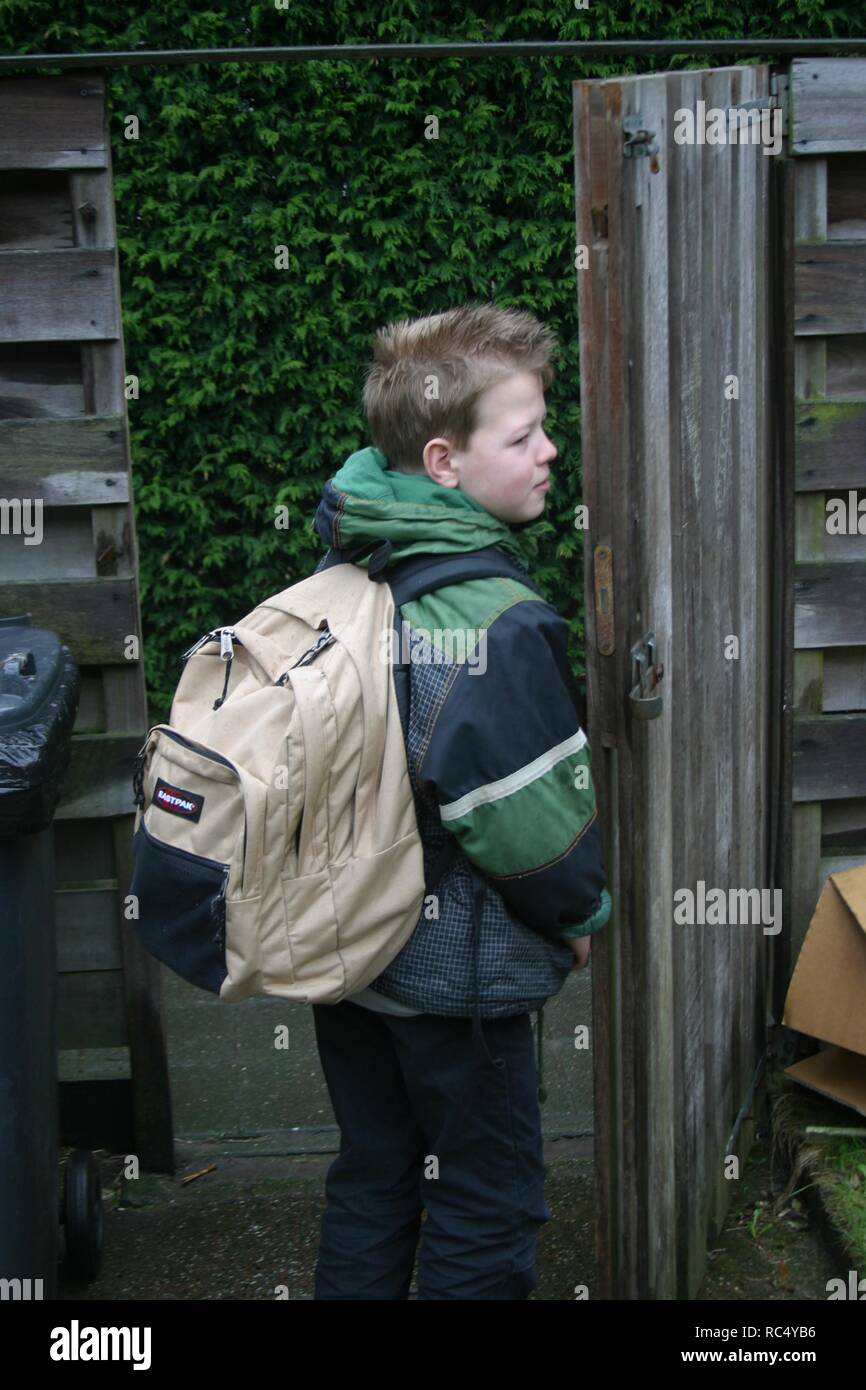Elementary boy with back-pack standing at the gate, waiting for school drop-off. Stock Photo