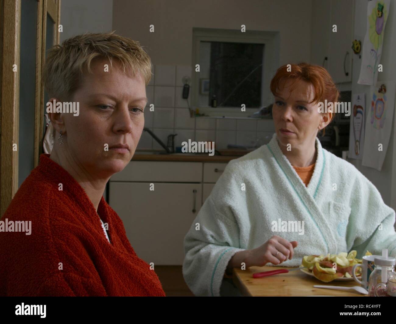 Two adult women sit at table in housecoat and discuss or argue at home. Stock Photo
