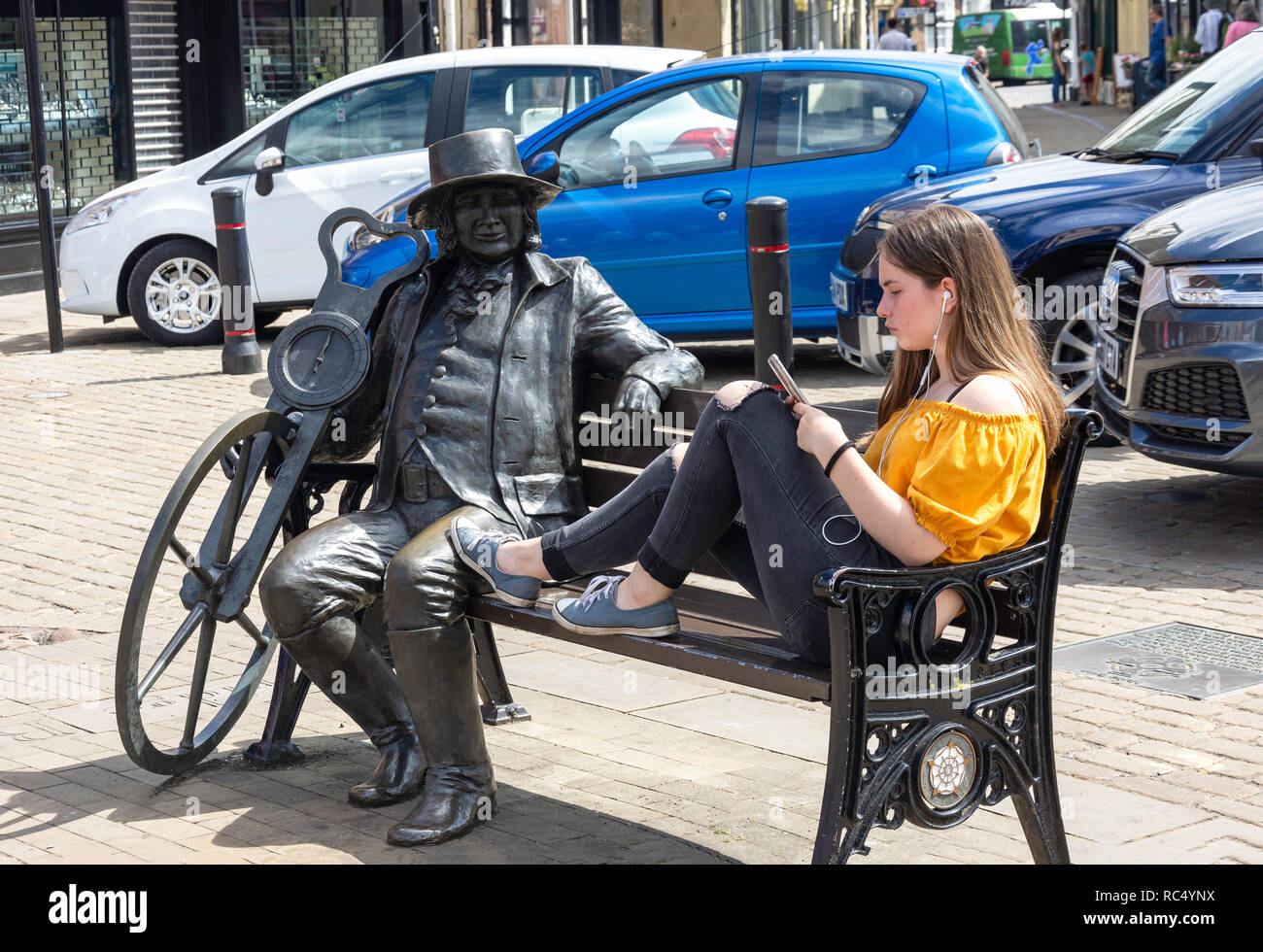 Young woman sitting on bench with historical figure, Market Place, Knaresborough, North Yorkshire, England, United Kingdom Stock Photo