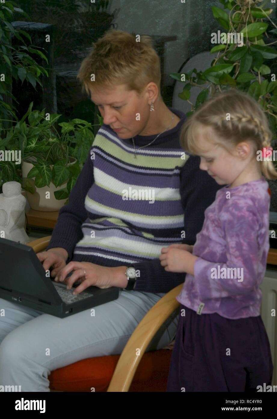 Mother engaged with laptop in the 2000s, no time to play with her daughter. Stock Photo