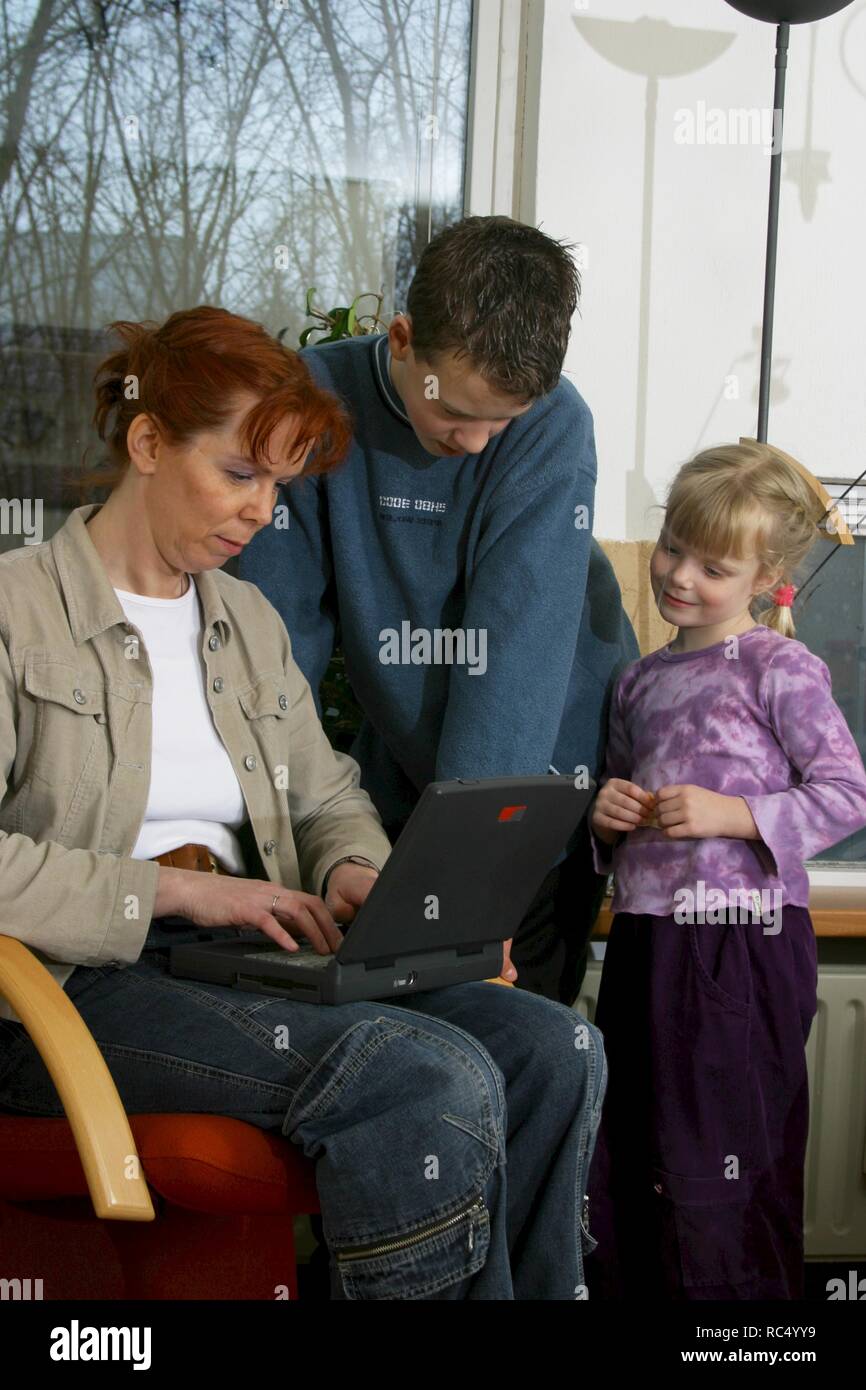 2003: Mother and 2 children curious looking at laptop on lap. Stock Photo