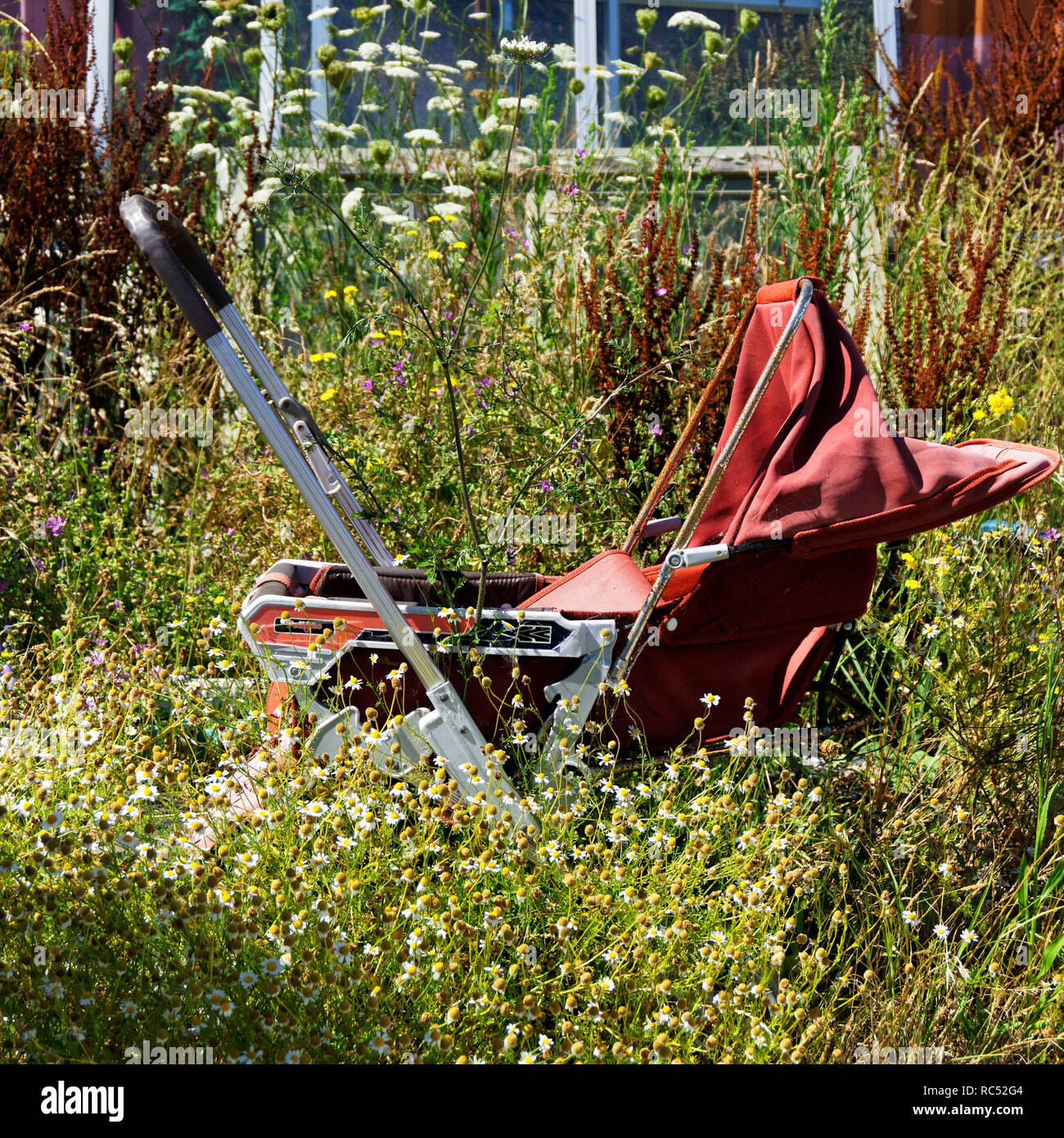 The kids have grown up so throw the pram away. Pram dumped or abandoned on waste ground. Stock Photo