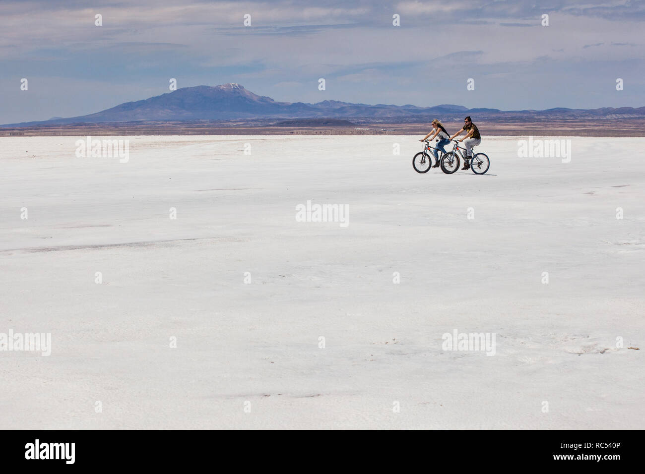 A young couple set out on the adventure of a lifetime as they cycle across the vast and open Salar de Uyuni enjoying freedom and beautiful views. Stock Photo
