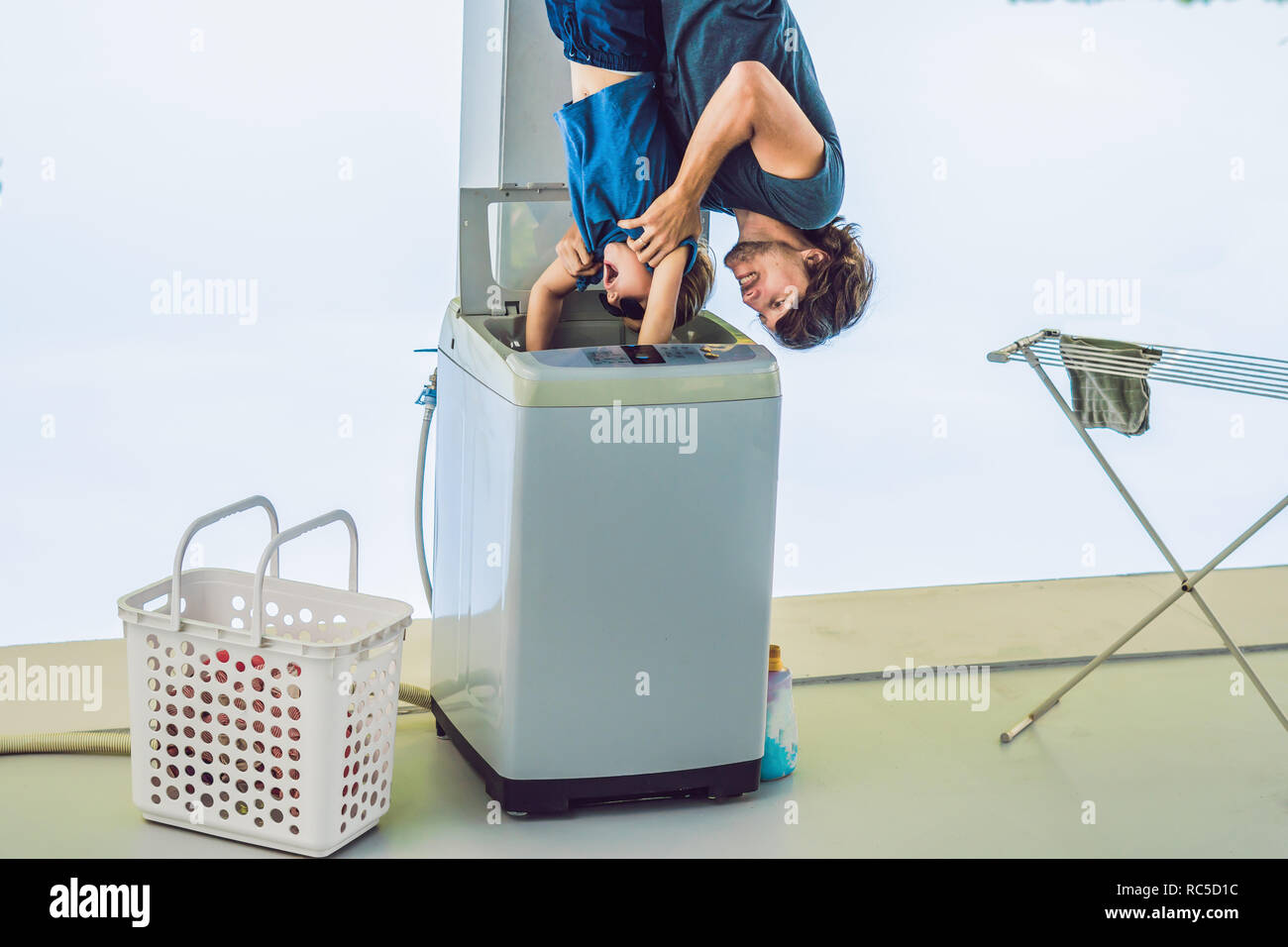Father tries to wash his son in a washing machine standing upside down with his feet Stock Photo