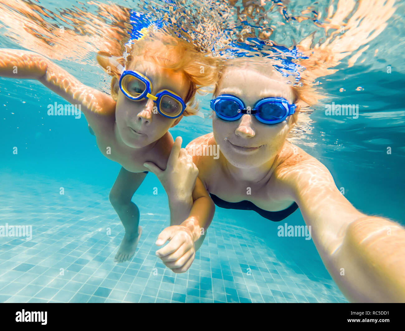 Mom and son in diving glasses swim in the pool under the water Stock
