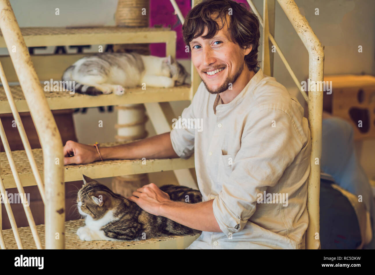 Portrait of handsome young man playing with cat and drinks coffee Stock Photo