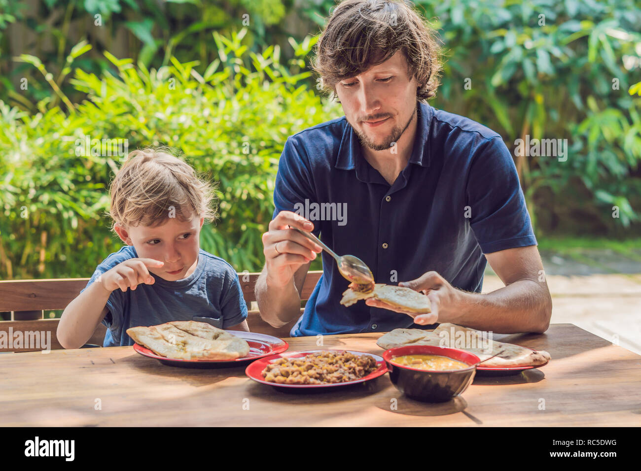 Father and son try Indian food in a cafe on the street Stock Photo